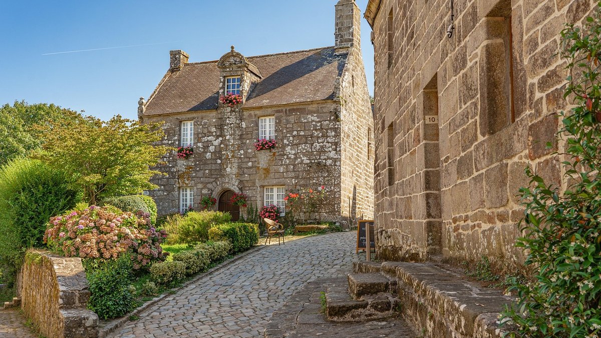 Ruelle pavée d'un village français avec maisons en pierre et jardins fleuris - Immobilier Voiron